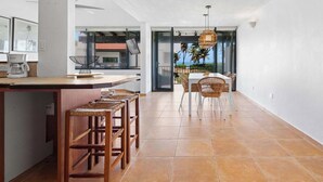A modern kitchen with a bar area, wooden stools, and a view of the ocean through large windows. - Playa Collect | Beachfront Haven w. Pool (Río Grande)