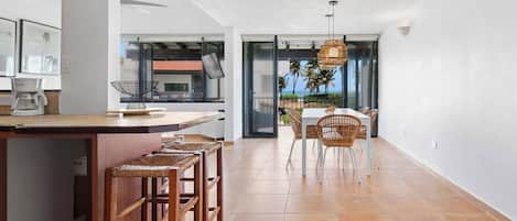 A modern kitchen with a bar area, wooden stools, and a view of the ocean through large windows.