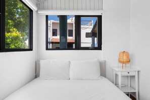 Una stanza bianca con un letto, una finestra e un piccolo tavolo con una sedia in vimini.