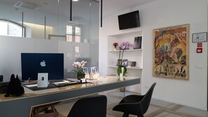 Een receptiebalie met een Apple iMac, een zwarte stoel en een poster aan de muur.