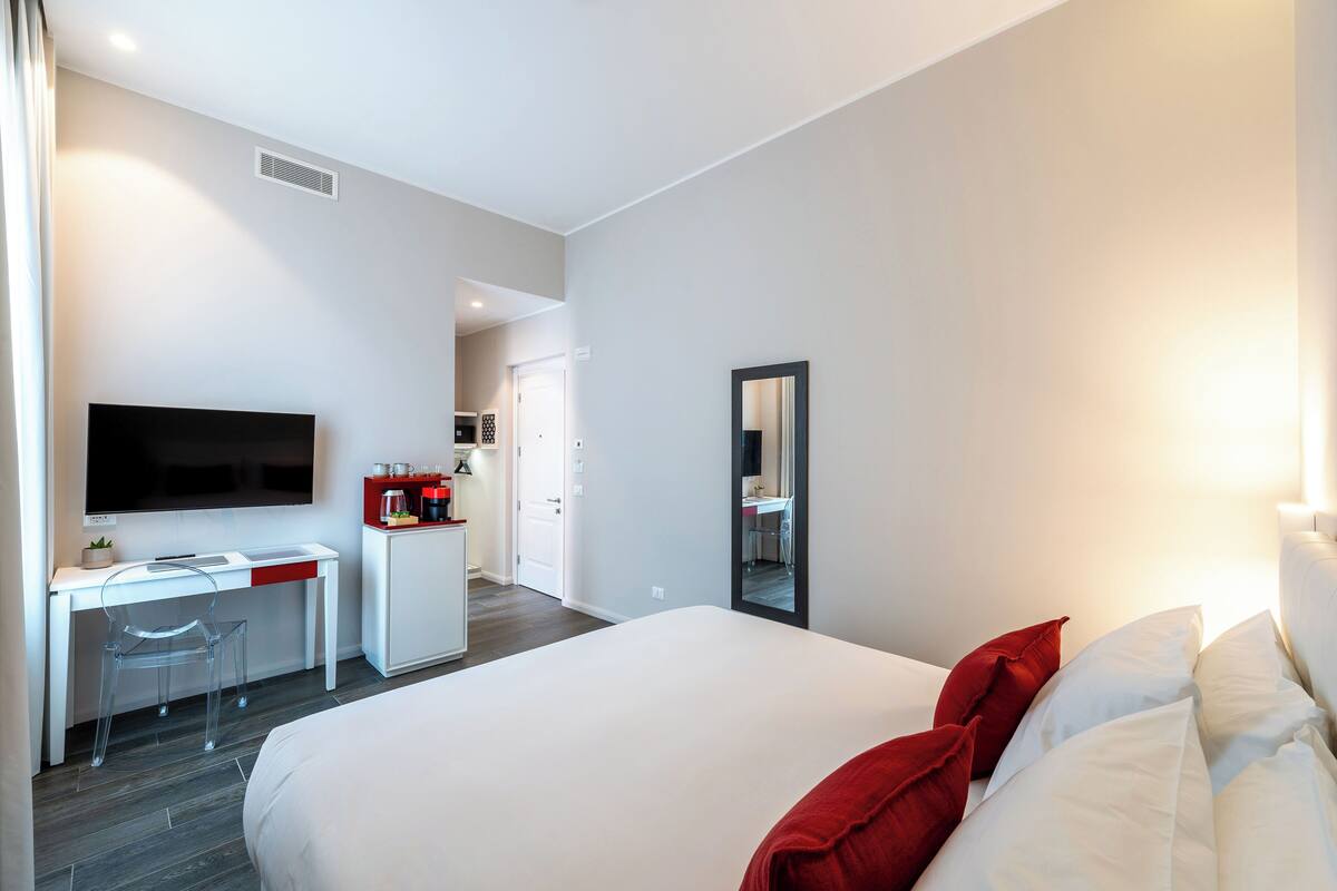 Ein modernes Hotelzimmer mit einem großen Bett, einem Schreibtisch mit Stuhl, einem Flachbildfernseher und einer kleinen Küchenzeile.
