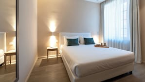Een hotelkamer met een groot bed, nachtkastjes, een spiegel en een raam met gordijnen.