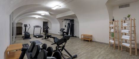 Un gimnasio con cintas de correr, máquinas de pesas y un banco de madera.