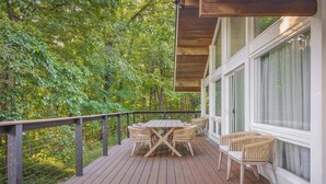 A wooden deck with a table and chairs, surrounded by greenery. - Windrush: Indoor Pool/Hot Tub/Sauna/Arcade (Columbus)