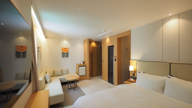 A hotel room with two beds, a sofa, a small table, a mirror, and a wall-mounted lamp. - Daisy Hotel (Tongyeong)