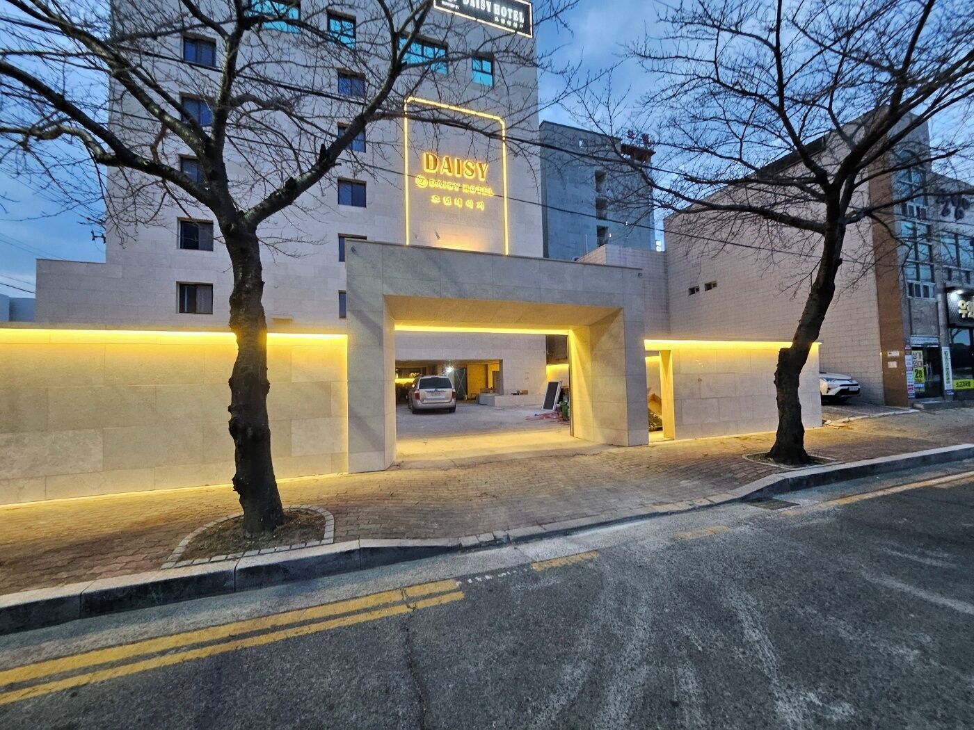 A modern hotel entrance with a neon sign, a covered parking area, and a building facade.