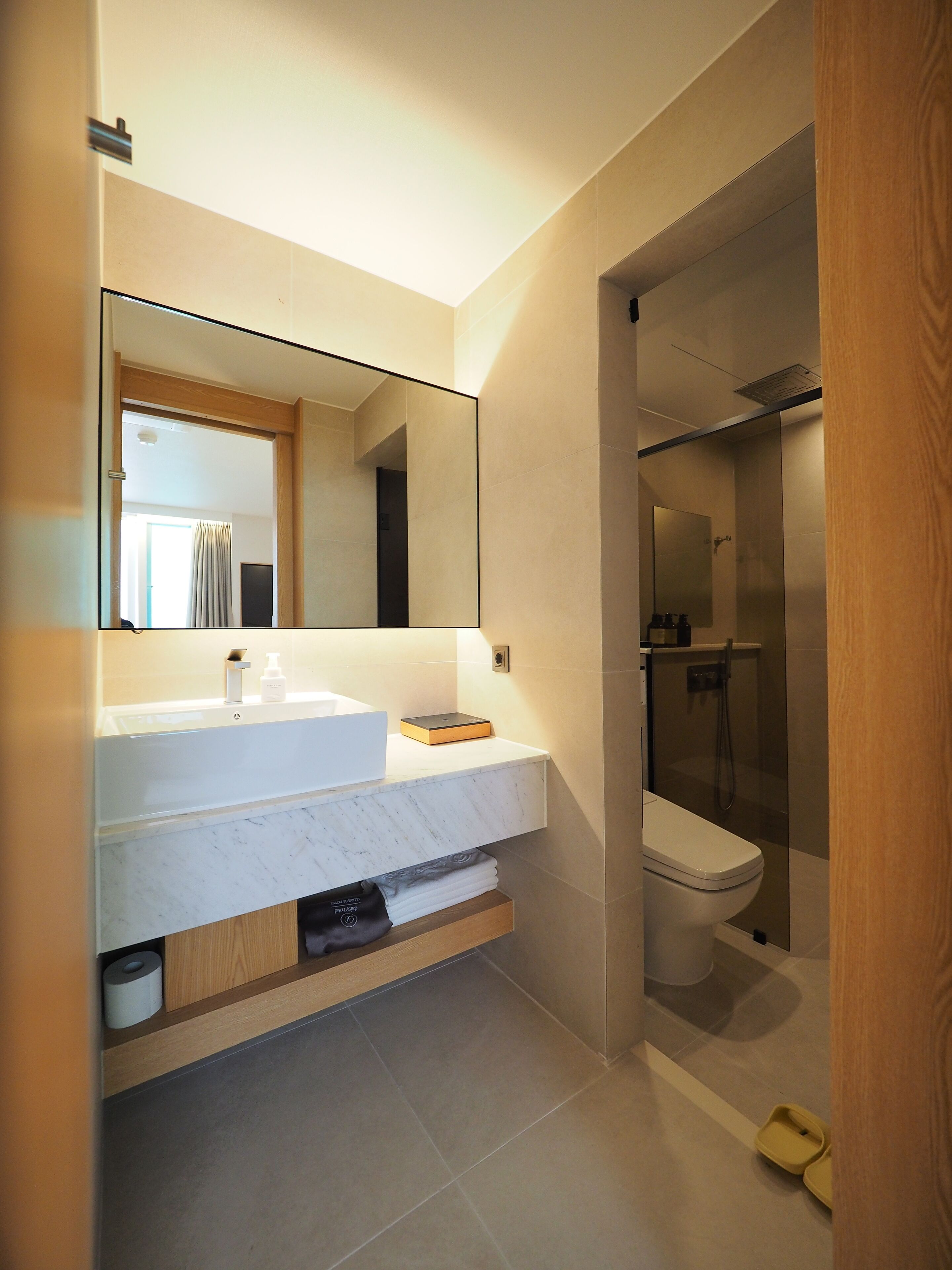 A modern bathroom with a white marble sink, a large mirror, and a glass-enclosed shower.