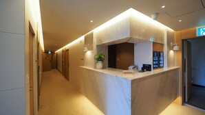 A hotel reception area with a marble counter, a potted plant, a digital information board, and a visible exit sign. - Daisy Hotel (Tongyeong)