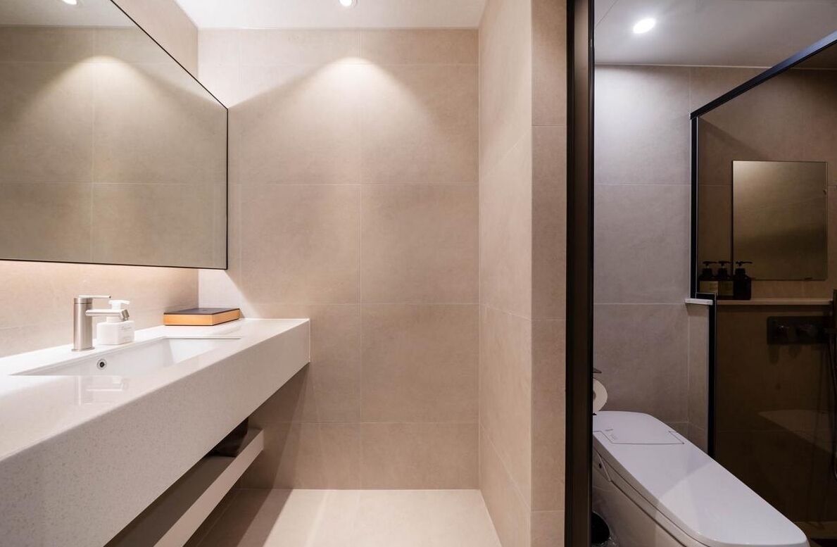 Un baño moderno con un espejo grande, un lavabo blanco y una cabina de ducha de vidrio.