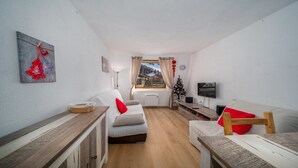 Een gezellige woonkamer met een bank, een kleine tafel, een televisie en een raam met uitzicht op een besneeerd landschap.