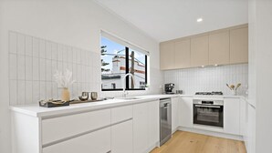 Une cuisine moderne avec des meubles blancs, un plancher en bois et une fenêtre donnant sur des immeubles.