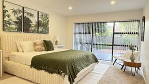 Une chambre dotée d’un grand lit, offrant une vue sur l’extérieur grâce à une porte coulissante, et agrémentée d’œuvres d’art au mur.