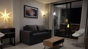 A modern living room with a dark sofa, a wooden coffee table, a star-shaped lamp, a framed picture of a bridge, and a view of a balcony with a dining area. - Villa Milá A3- Luxury sunset view - Close to everything (Salento)