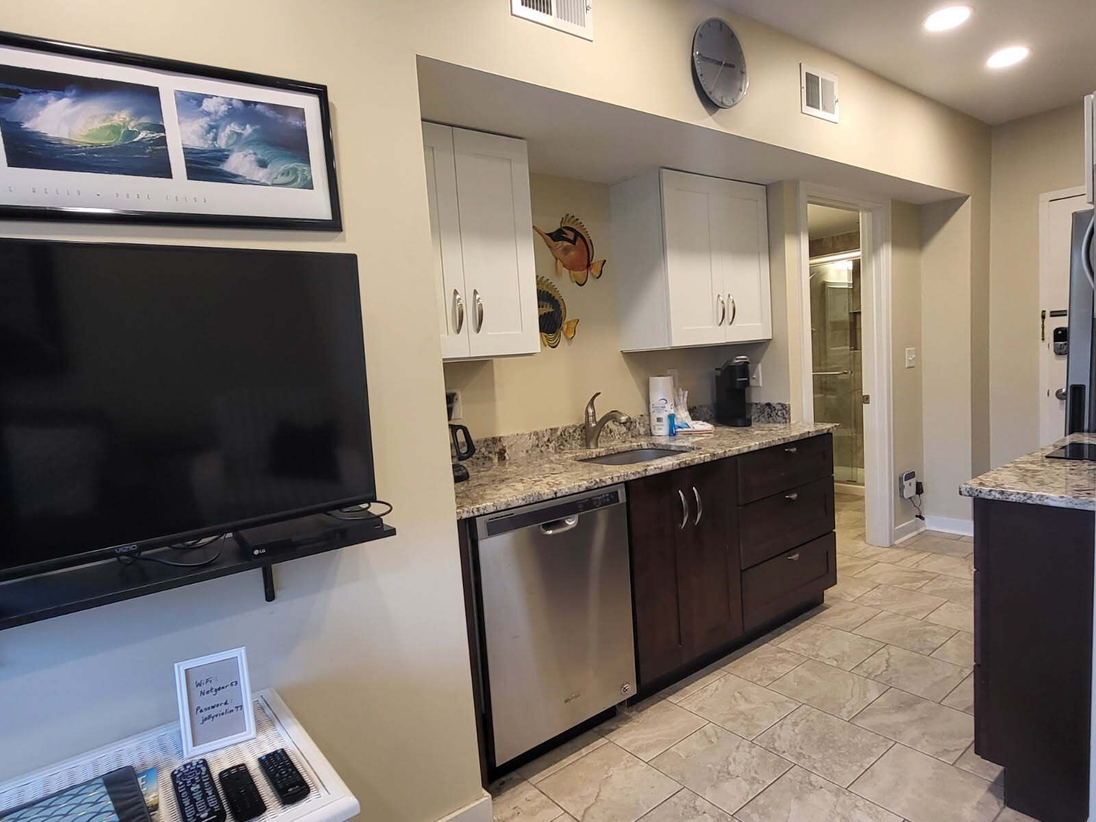 A modern kitchen with a flat-screen TV, built-in dishwasher, and granite countertops.