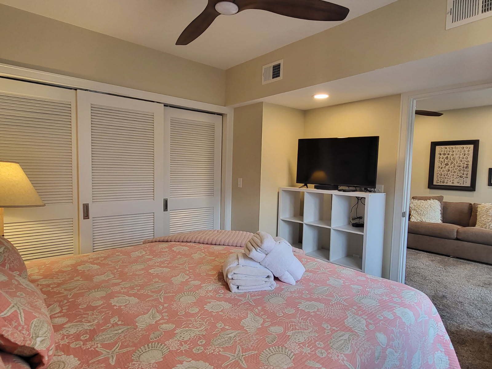 A bedroom with a bed, a TV, a ceiling fan, and a closet.