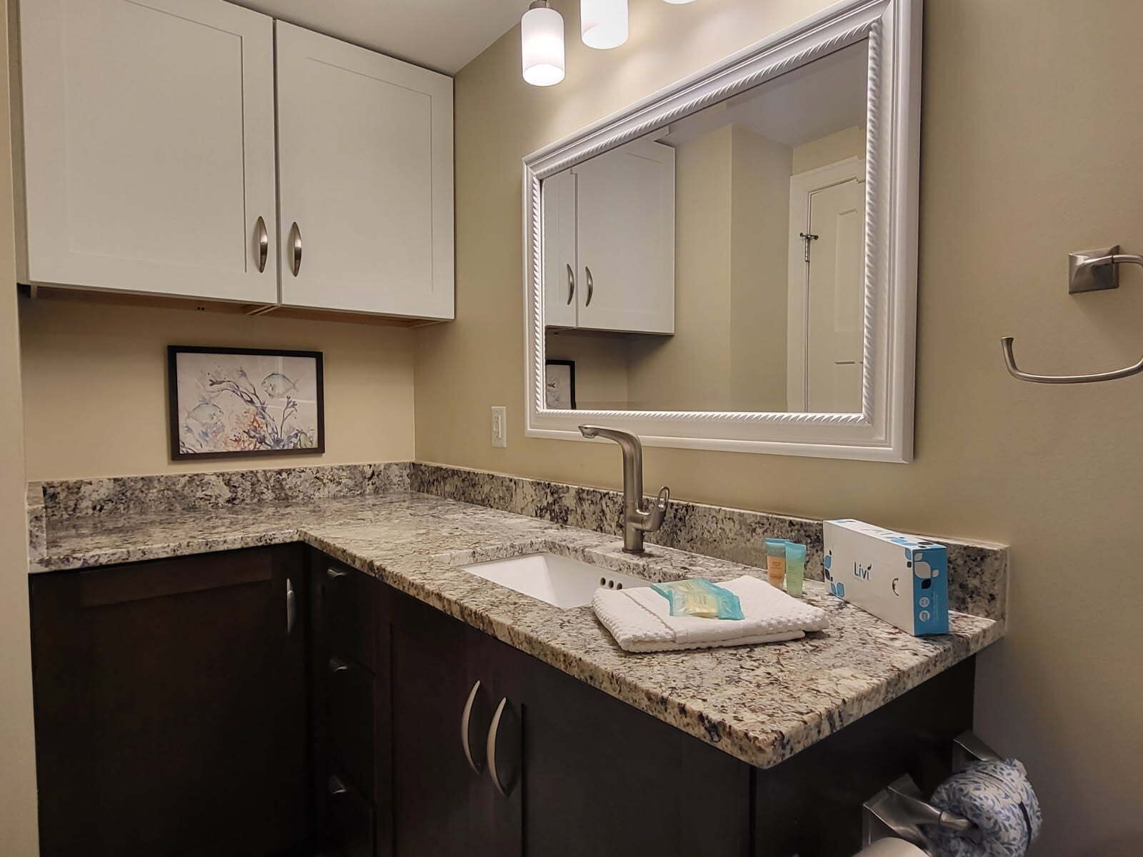 A bathroom with a granite countertop, a sink, a large mirror, and cabinets.