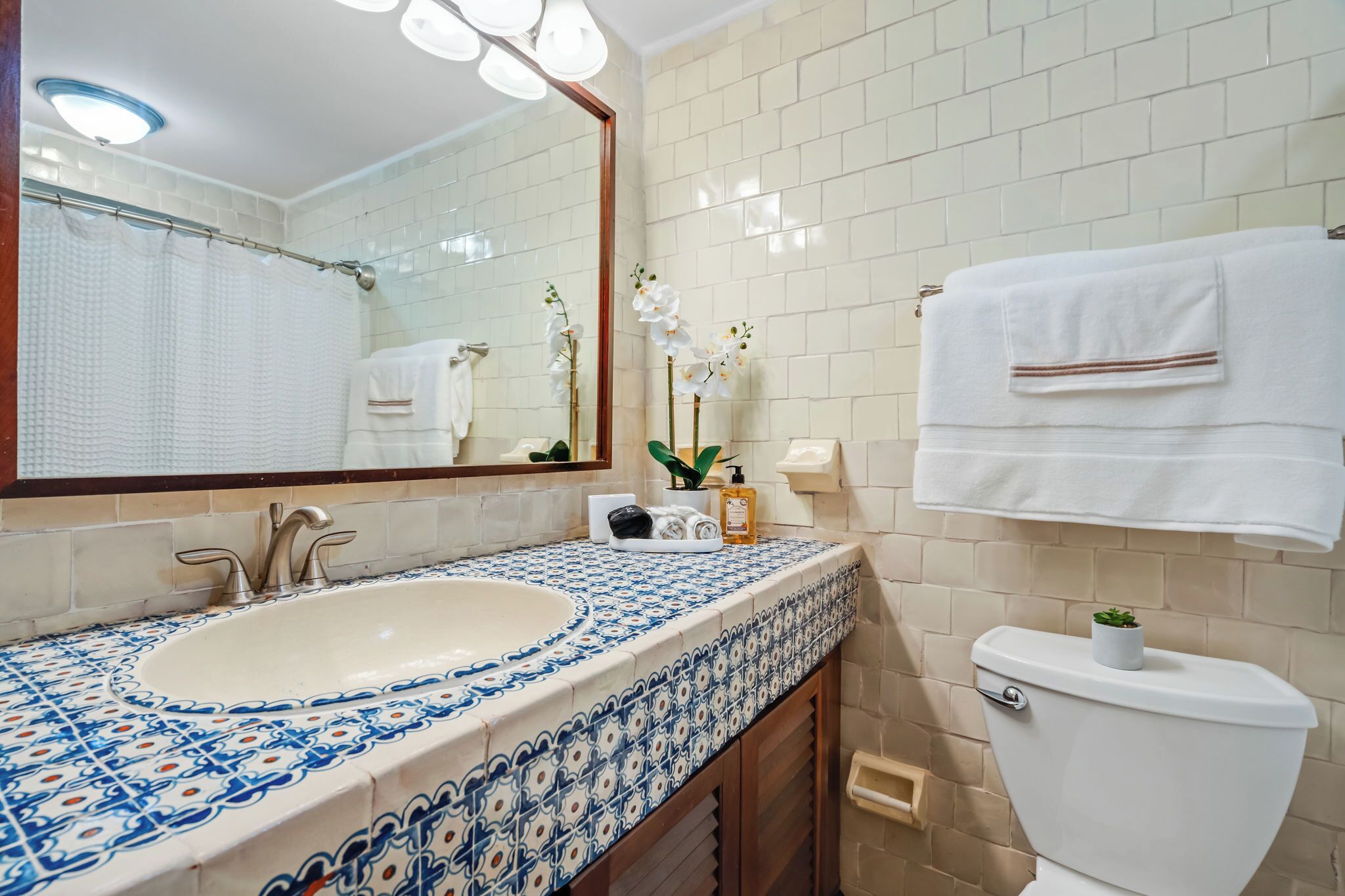A bathroom with a white sink, blue and white patterned tiles, a mirror, a toilet, and a towel rack.