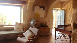 A cozy room with a stone wall, a wooden table, a cushioned bench, and a fan. - Farmhouse With Pool and Valley Views (Munxar)