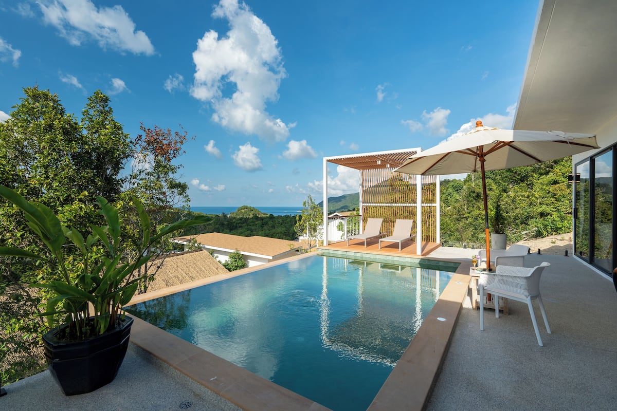 A modern outdoor pool area with a clear view of the ocean, a covered seating area, and a potted plant.