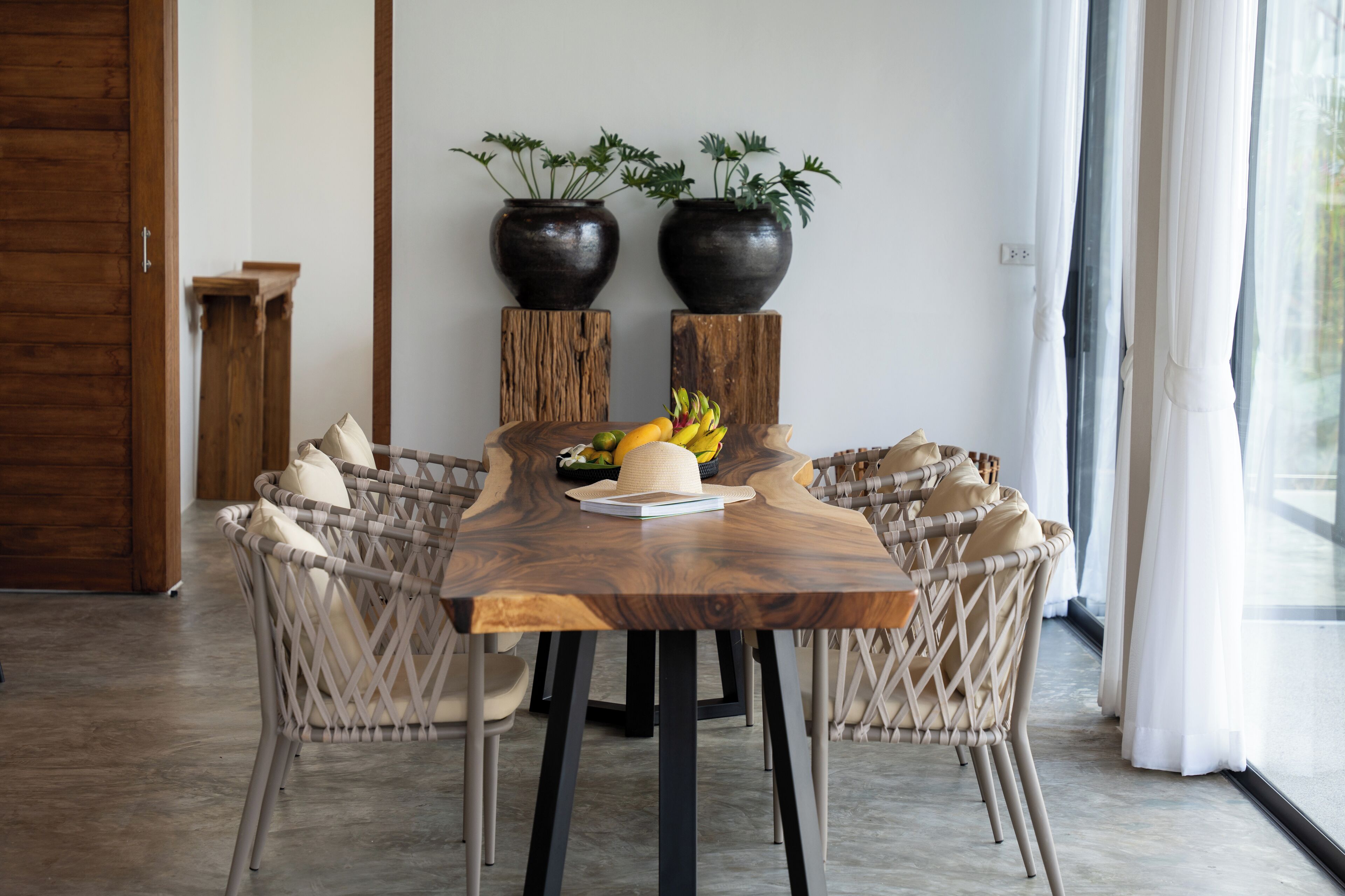 A dining area with a wooden table, wicker chairs, and potted plants.