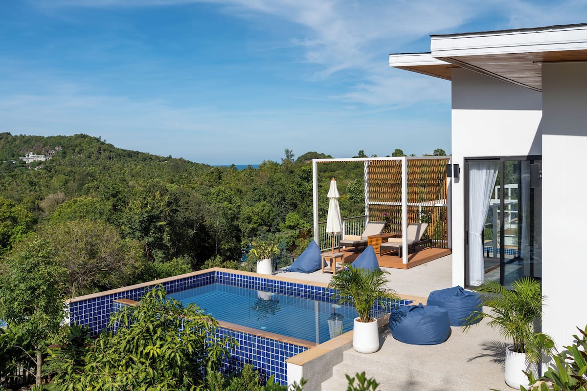 A modern pool area with a clear view of the surrounding forest and a hillside.