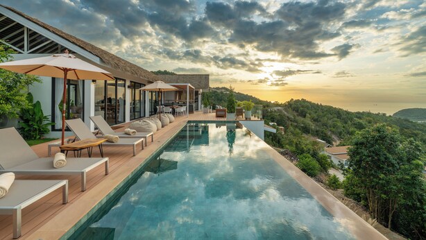 Zona de piscina con sillones de descanso y sombrillas, con vistas a un paisaje pintoresco.