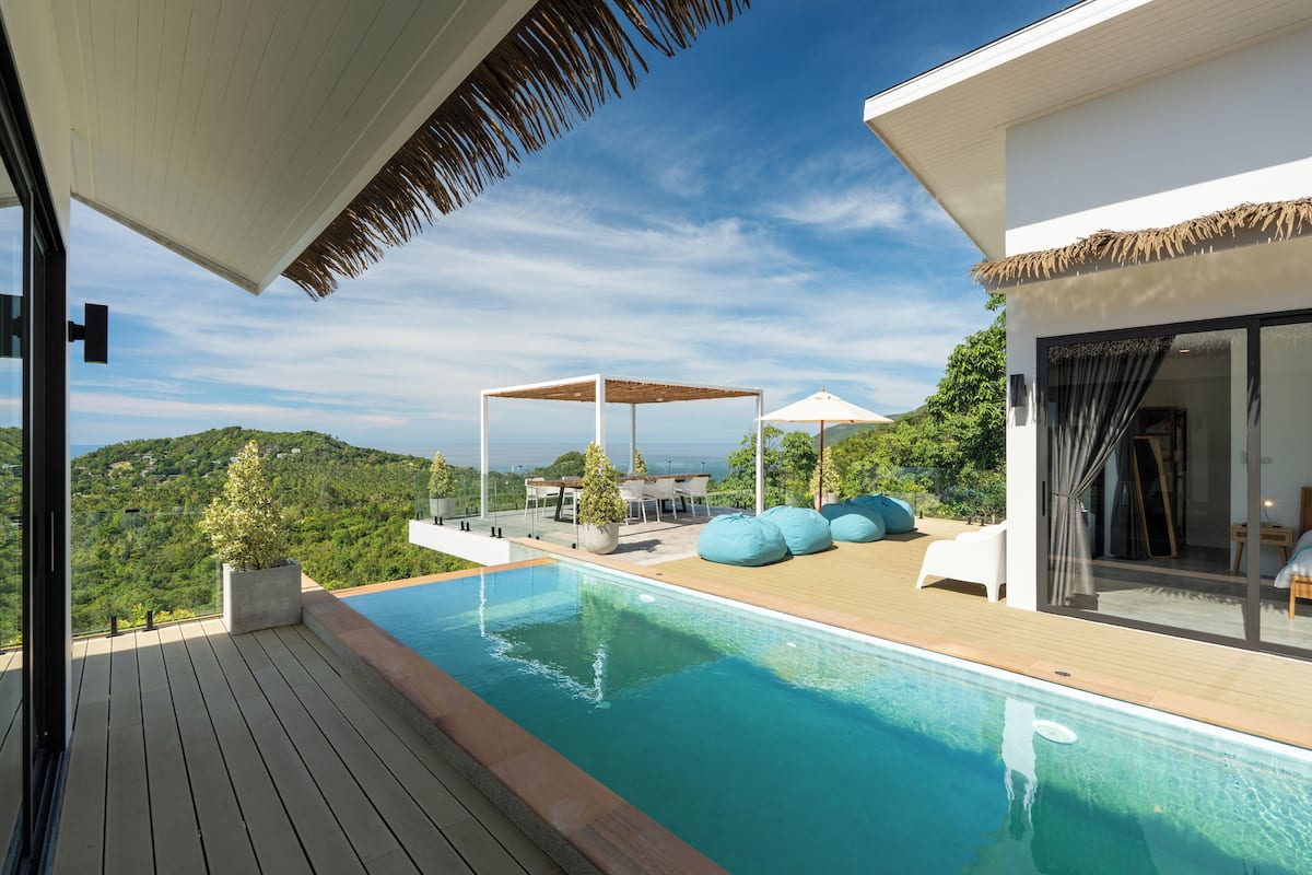 A modern outdoor pool area with a wooden deck, a lounge with blue bean bags, and a covered seating area.