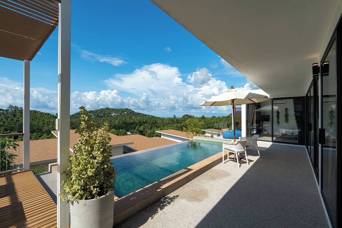 A modern outdoor pool area with a clear view of the surrounding landscape, a seating area with umbrellas, and a potted plant.