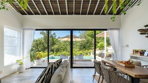 Amplia sala de estar con un gran ventanal corredizo que da a una piscina, una mesa de comedor de madera y un sofá confortable.