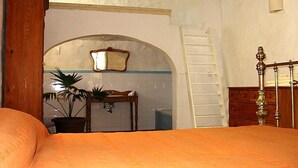 Une chambre à coucher comprenant un lit, une armoire en bois, une commode, un miroir, une plante en pot et une porte donnant sur une autre pièce.
