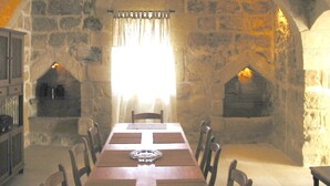 Une salle à manger aux murs de pierre, avec une longue table, des chaises et deux cheminées.
