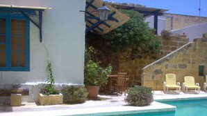 Un espace aménagé au bord de la piscine, avec un mur en pierre, une table en bois, des chaises et des plantes en pot.
