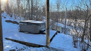 En træterrasse med jacuzzi under en pergola i træ, omgivet af sne og træer.