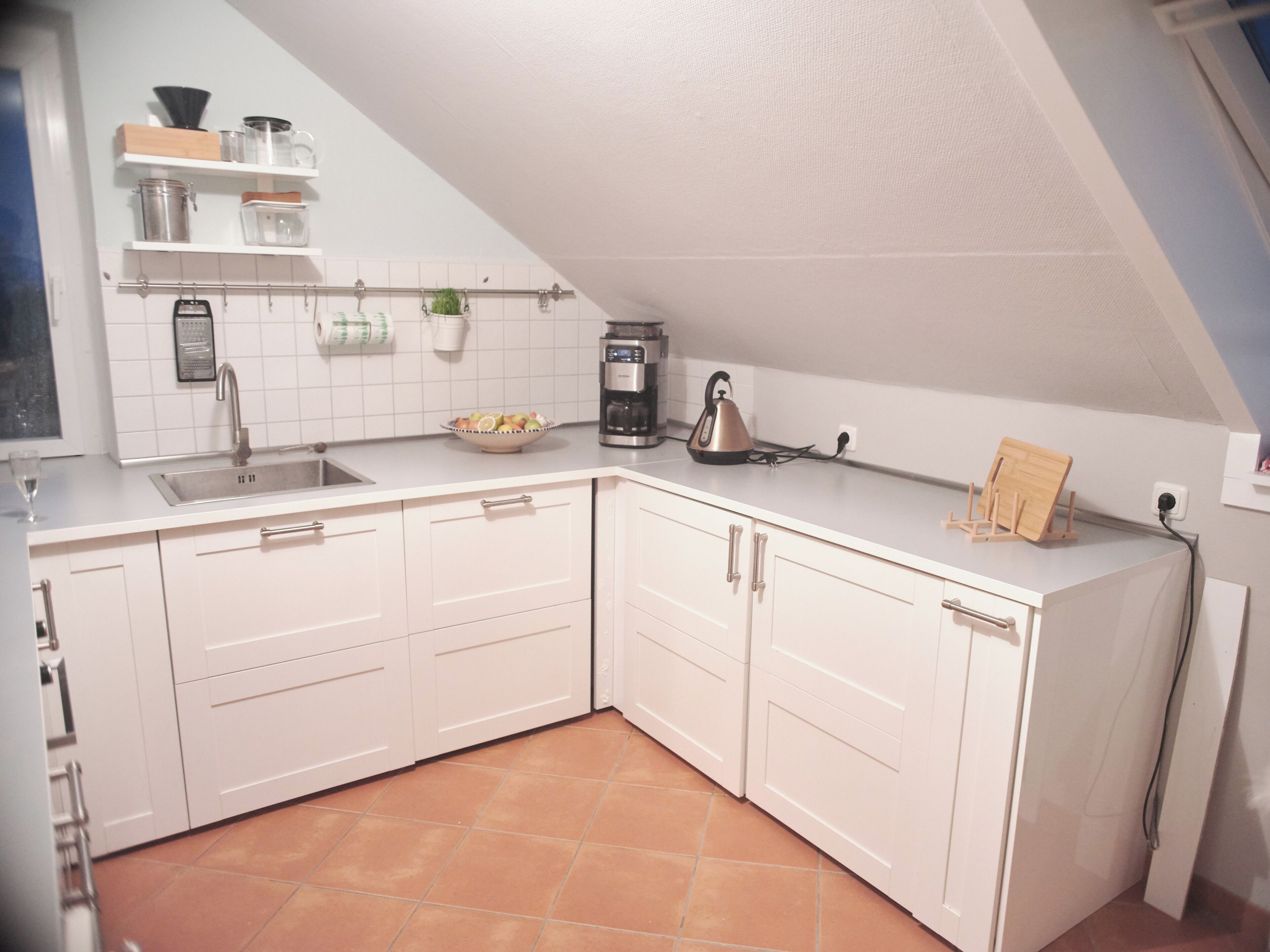 Una cucina con mobili bianchi, un lavandino, una macchina da caffè e un bollitore.