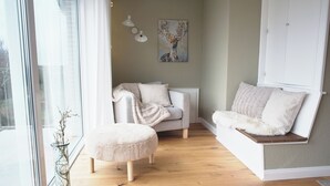 A cozy living room with a sofa, ottoman, and a painting on the wall. - Modern, spacious top-floor apartment with panoramic views of the Elbe (Hollern-Twielenfleth)