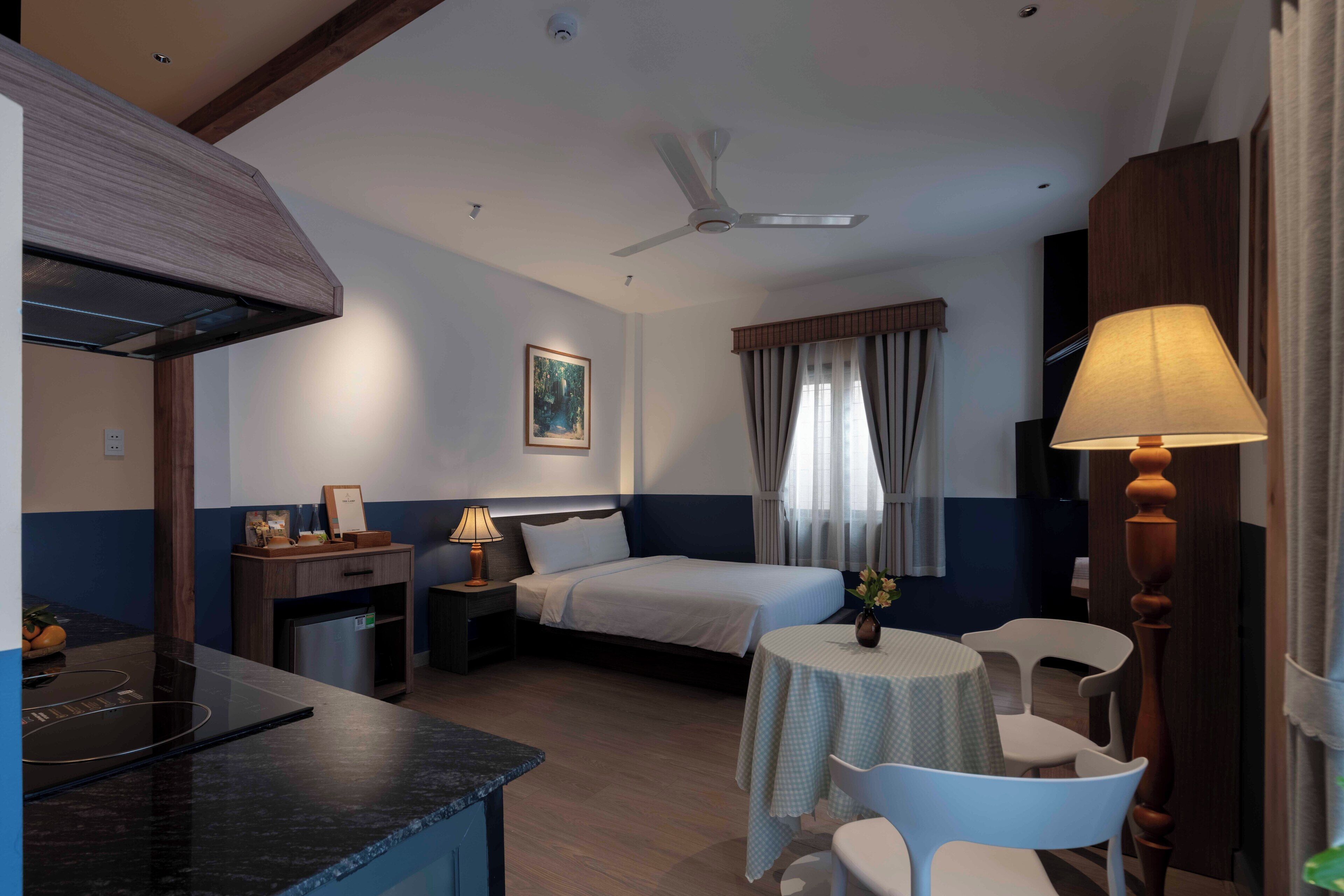 Une chambre d’hôtel équipée d’un lit, d’un bureau, d’une chaise, d’une table, d’un ventilateur de plafond et d’une fenêtre avec des rideaux.