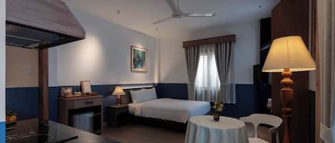 Une chambre d’hôtel équipée d’un lit, d’un bureau, d’une chaise, d’une table, d’un ventilateur de plafond et d’une fenêtre avec des rideaux.