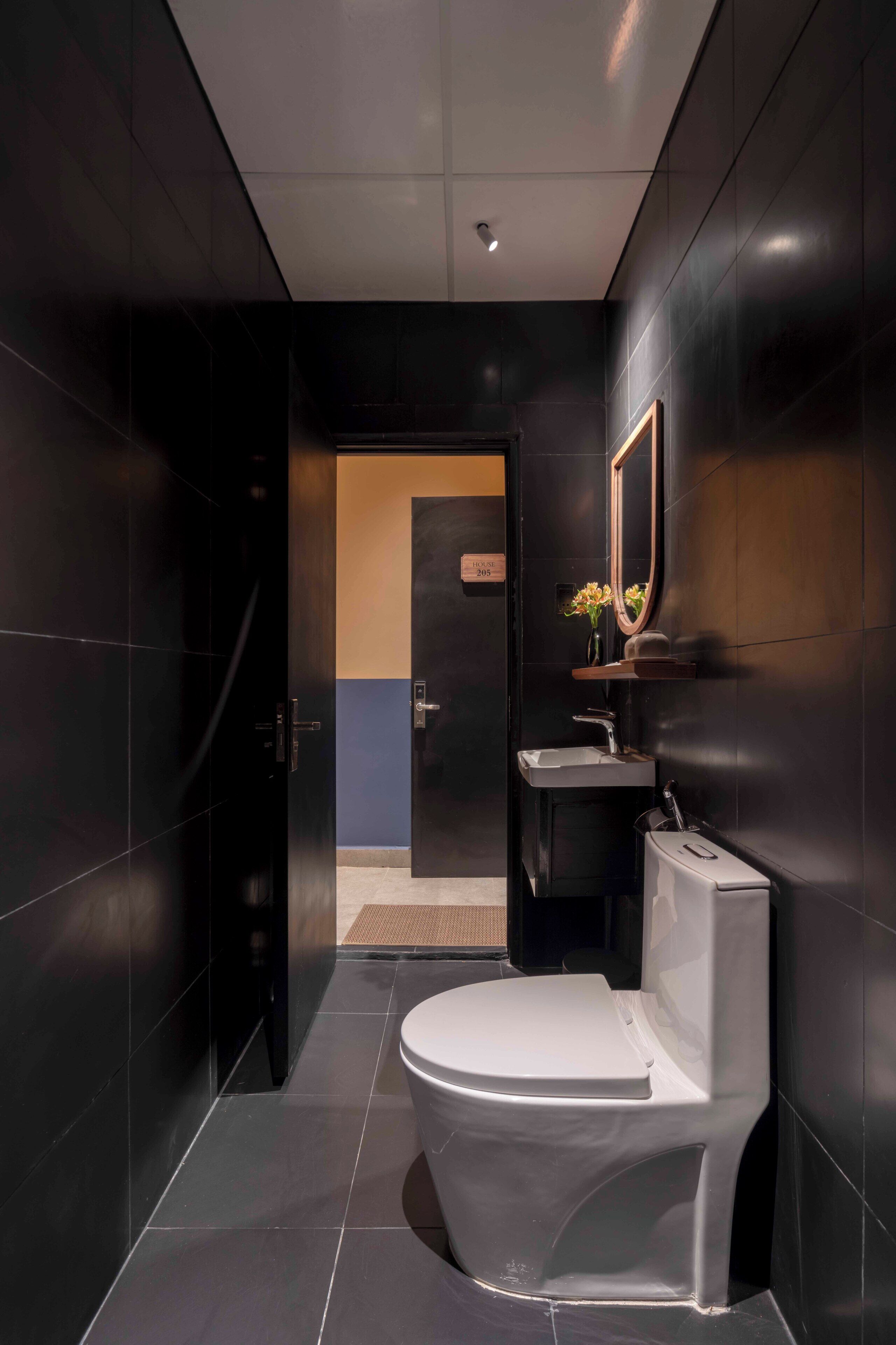 A modern bathroom with dark tiles, a white toilet, a sink, and a mirror.