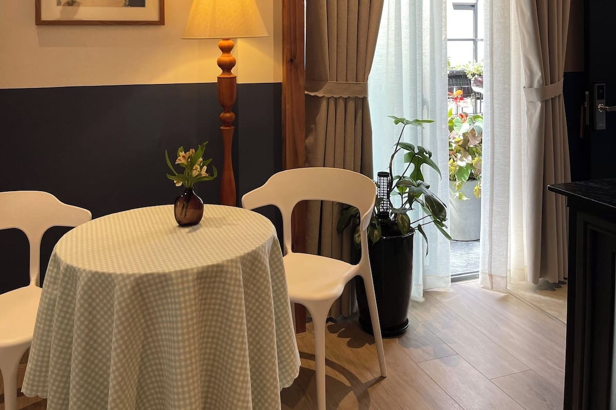 Un coin repas avec une table dressée pour deux personnes, une lampe et un tableau encadré au mur.