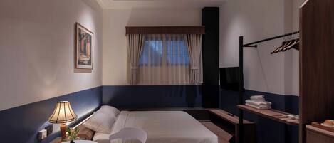 A hotel room with a bed, a bedside table with a lamp, a chair, a window with curtains, a coat rack, and a wardrobe.