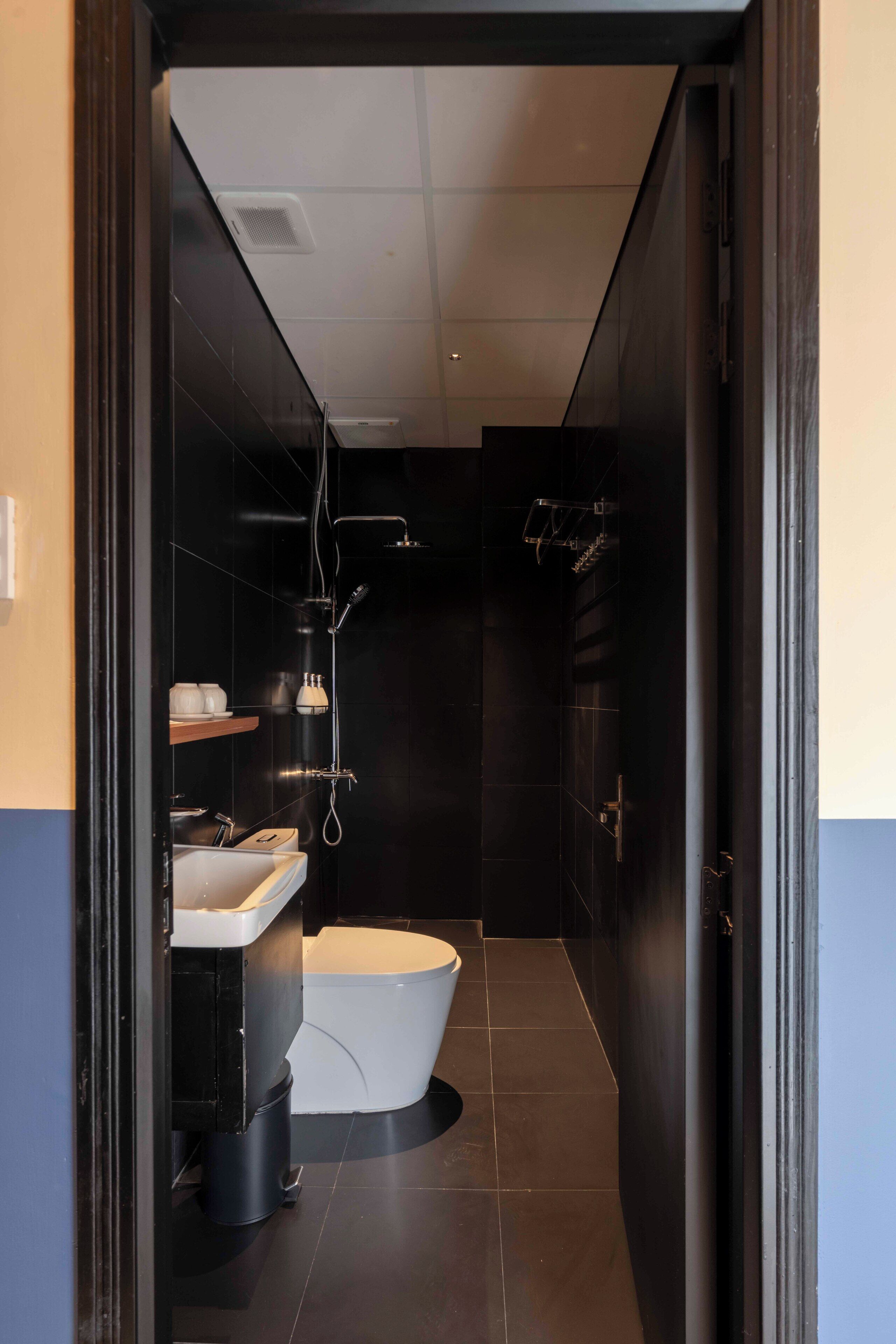 A modern bathroom with a white toilet, black tiles, a sink, and a shower.