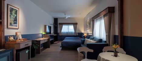 Habitación de hotel con cama, escritorio, silla, una mesita y televisor.