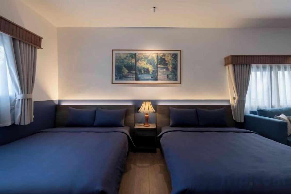 Una habitación de hotel con dos camas, una mesita de noche con lámpara y un cuadro en la pared.