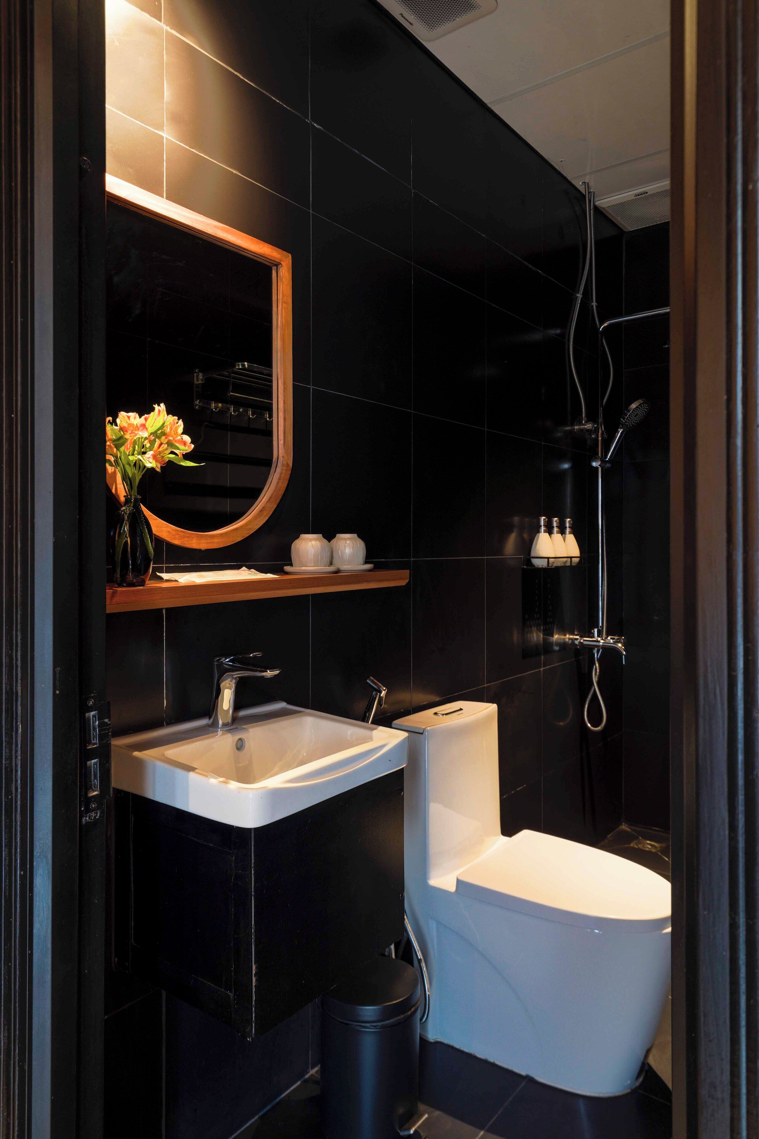 A modern bathroom with a black tiled wall, a white sink, a toilet, and a shower.