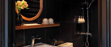 A modern bathroom with a black tiled wall, a white sink, a toilet, and a shower.