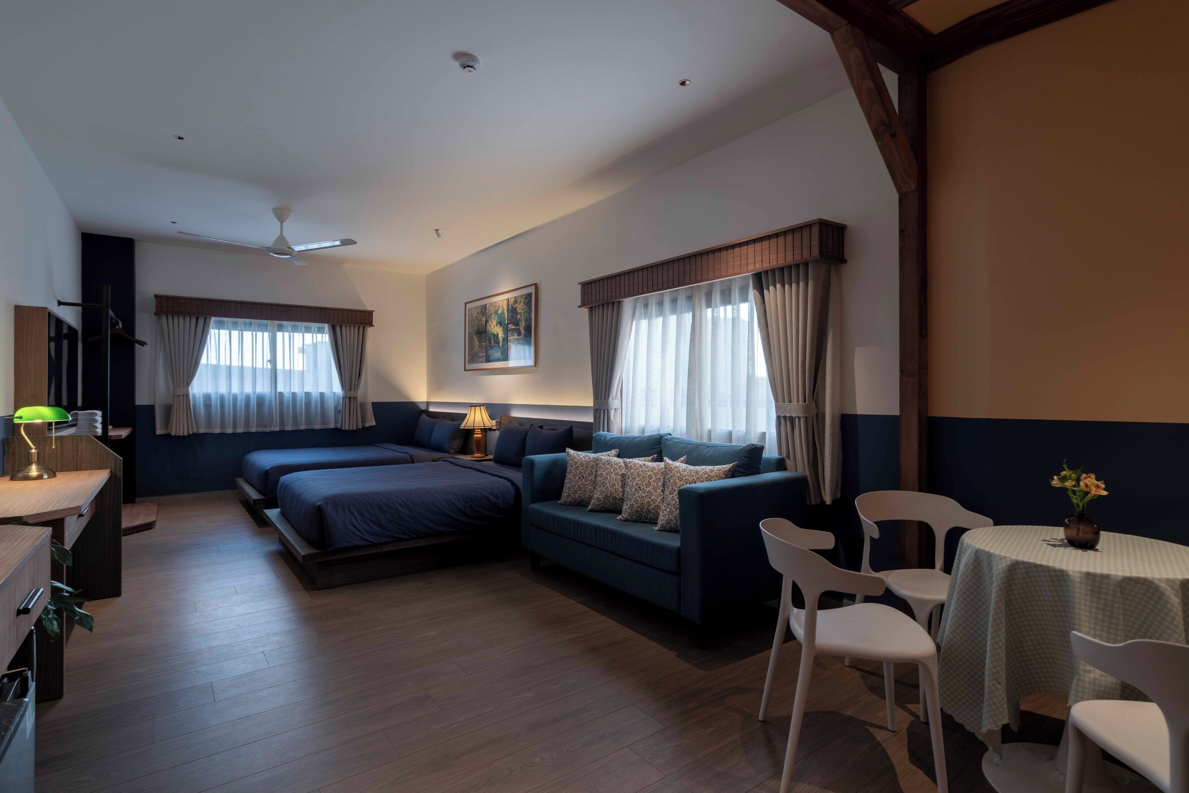 A modern hotel room with a bed, a sofa, a desk, and a dining area.