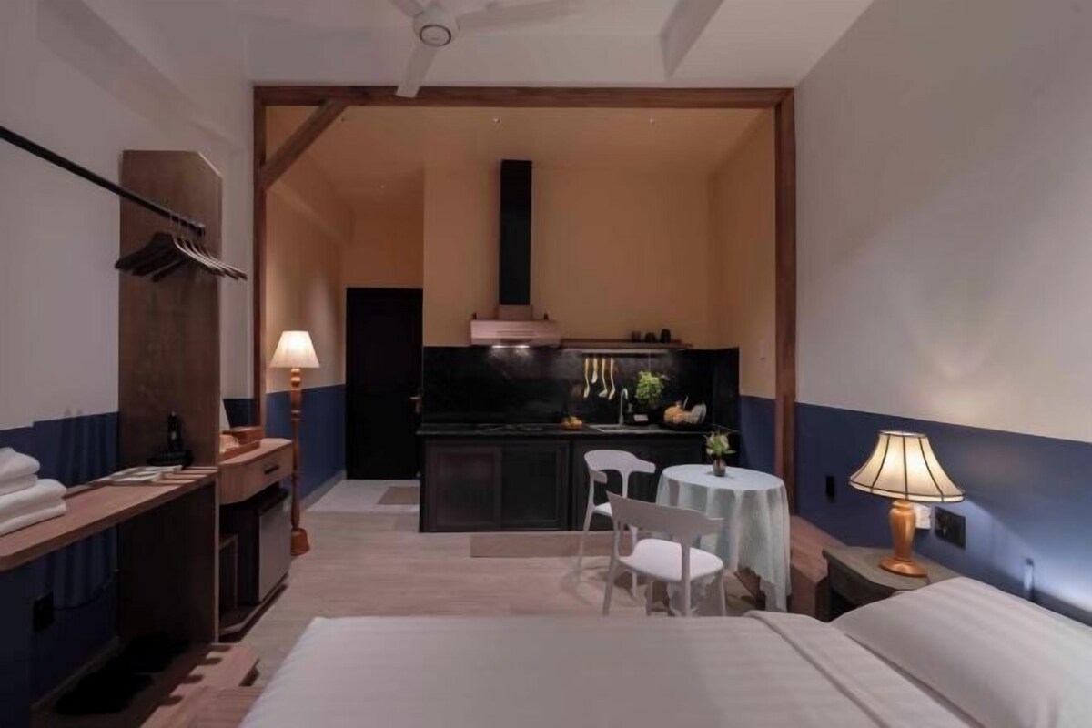 Habitación de hotel con cama, escritorio, silla, pequeña mesa y área de kitchenette.