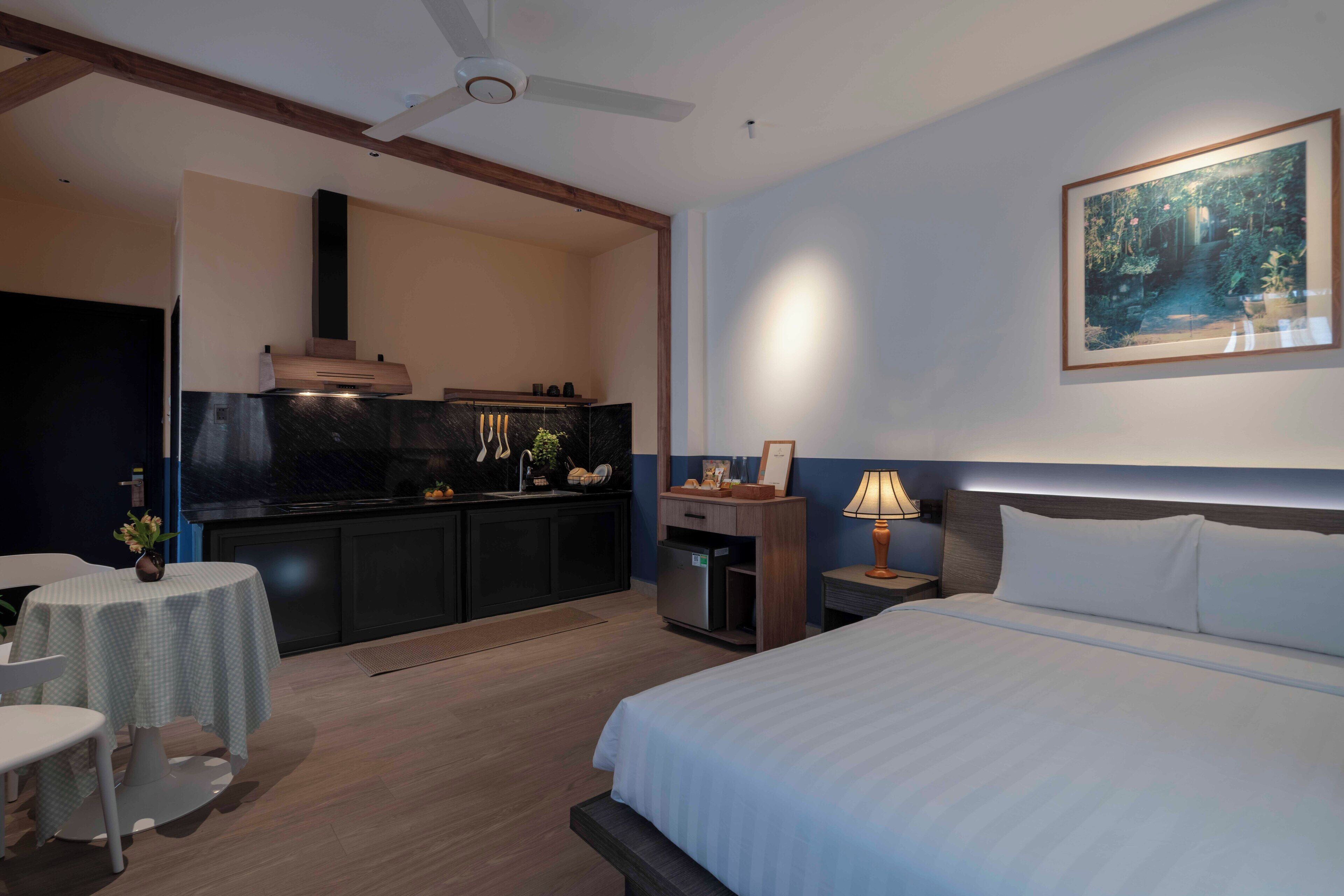 Una camera d'albergo con un letto, una scrivania, una sedia, un tavolino, un quadro e angolo cottura.