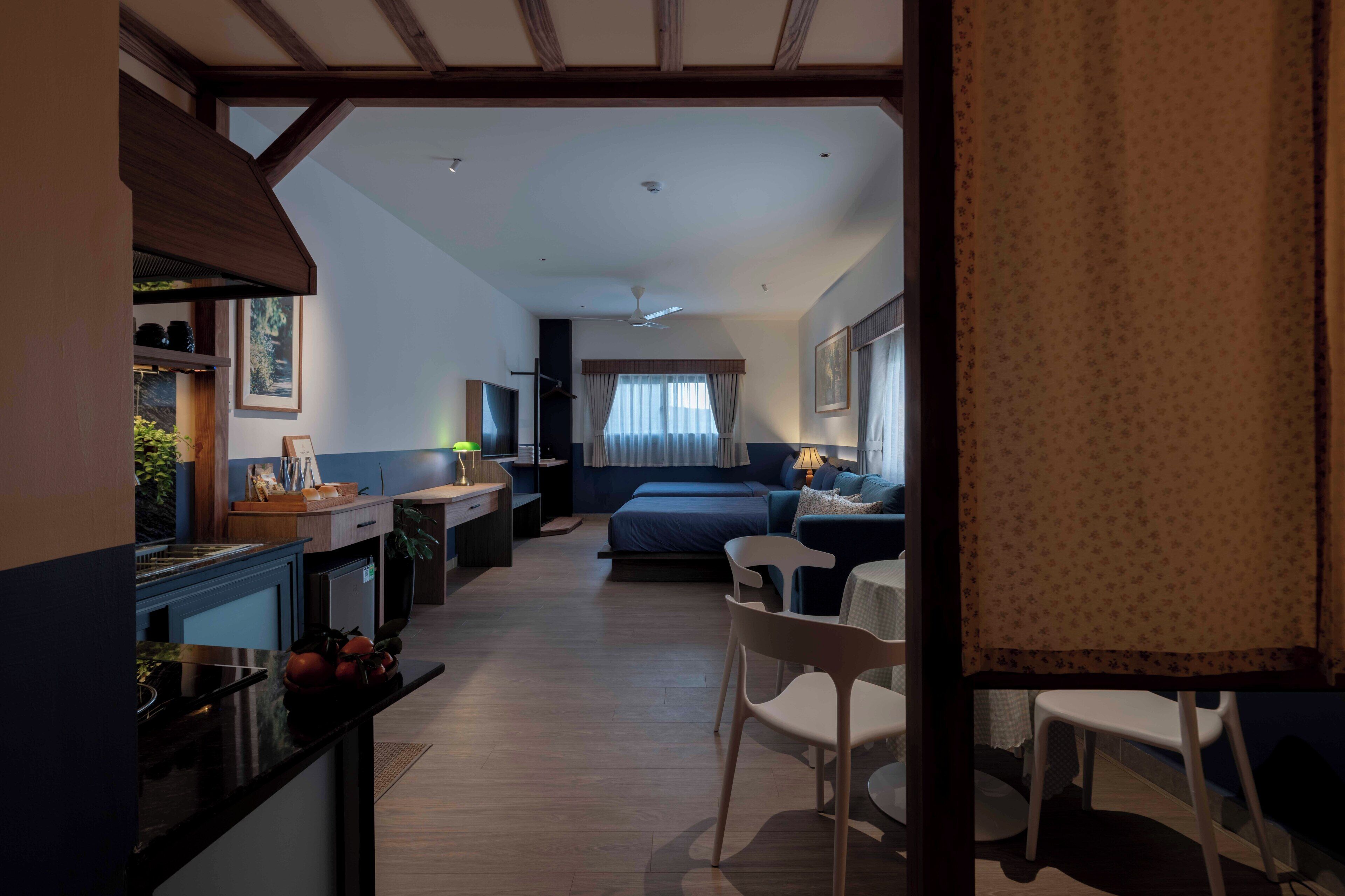 A compact hotel room with a kitchenette, a bed, a seating area, and a dining table.