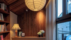 Een houten receptiebalie met een hanglamp, boekenkasten en een raam met uitzicht.